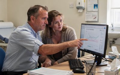 A consultant points at blood test charts on a computer screen as his patient, a woman with long covid, looks on in a clinic room